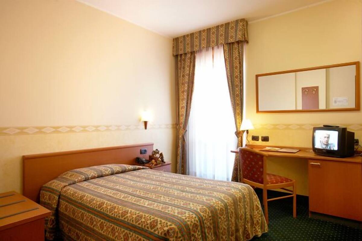 Una habitación de hotel con una cama, un escritorio con televisor, una silla y un espejo.