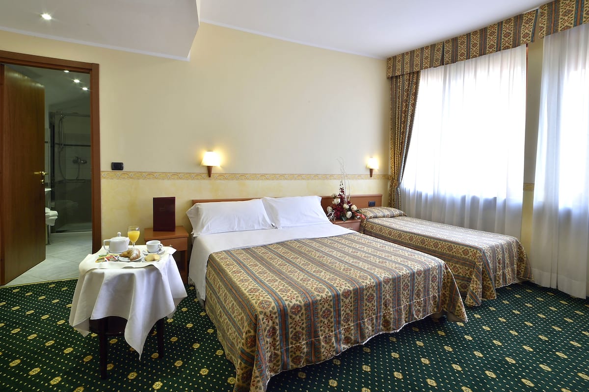 Habitación de hotel con dos camas, una mesita con alimentos para el desayuno y zona de ducha.