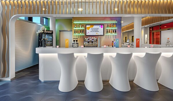 Una zona de bar moderna con una barra blanca, taburetes y diversas bebidas exhibidas en estanterías iluminadas.