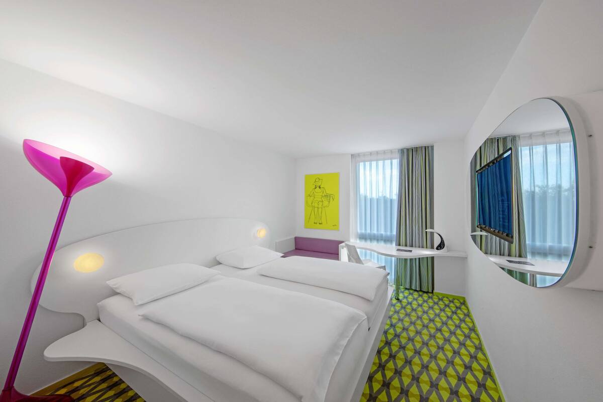 Une chambre d’hôtel moderne, équipée d’un lit, d’une table de chevet et d’un grand miroir.