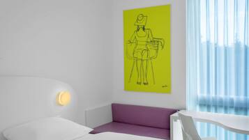 A modern hotel room with a white bed, a purple sofa, a white desk, and a bright yellow artwork on the wall.