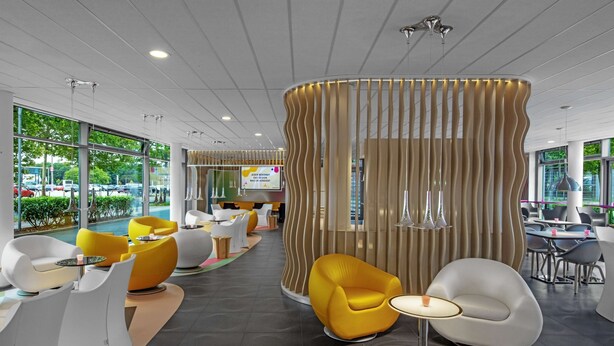 Ein modernes Interieur mit Sitzbereichen, einer zentralen Wandgestaltung und großen Fenstern mit Blick ins Freie.