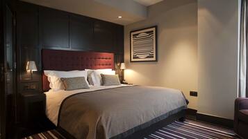 A hotel room with a large bed, dark wood headboard, two bedside tables with lamps, a framed artwork on the wall, and a striped carpet.