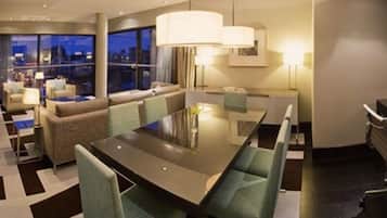 A modern hotel room with a dining area, a sofa, and a view of the cityscape at night.
