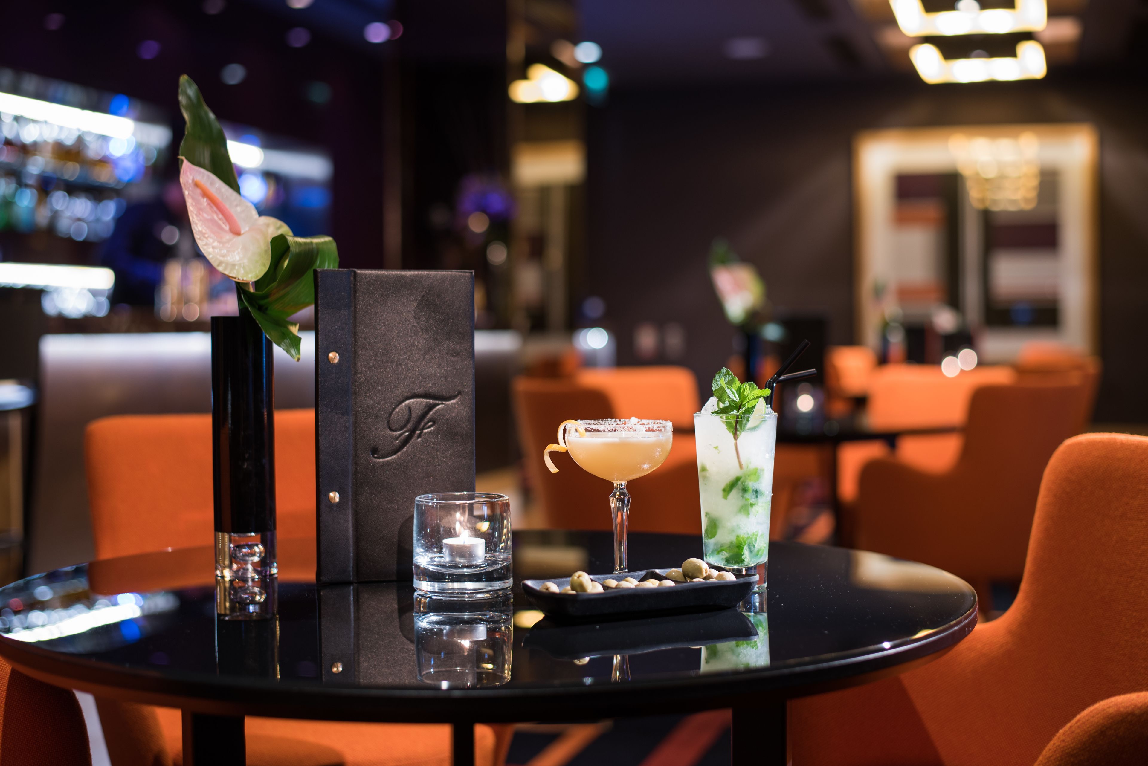A bar area with a cocktail, a glass of water, and a menu stand.