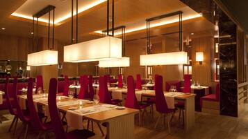 A restaurant with wooden tables and red chairs, illuminated by pendant lights.