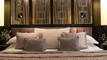 A neatly made bed with a large central pillow and two smaller pillows on either side, a headboard with a geometric design, and a nightstand with a glass of wine and a book.