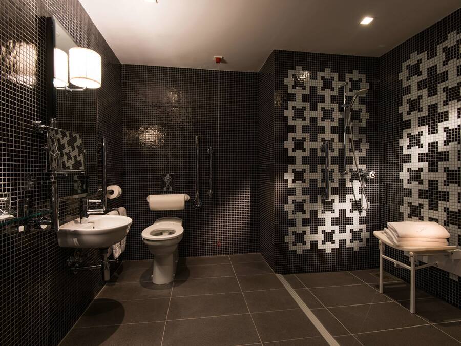 Un bany modern amb una paret revestida de rajoles negres i blanques, un lavabo, un vàter i una zona de dutxa.