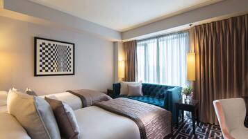 Habitación de hotel con una cama grande, un sofá más pequeño, una silla, una lámpara y una ventana con cortinas.