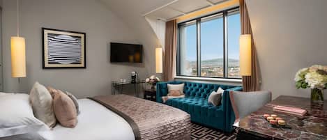 Habitación de hotel moderna con una cama grande, un sofá, un escritorio con una computadora portátil y vistas a la ciudad.