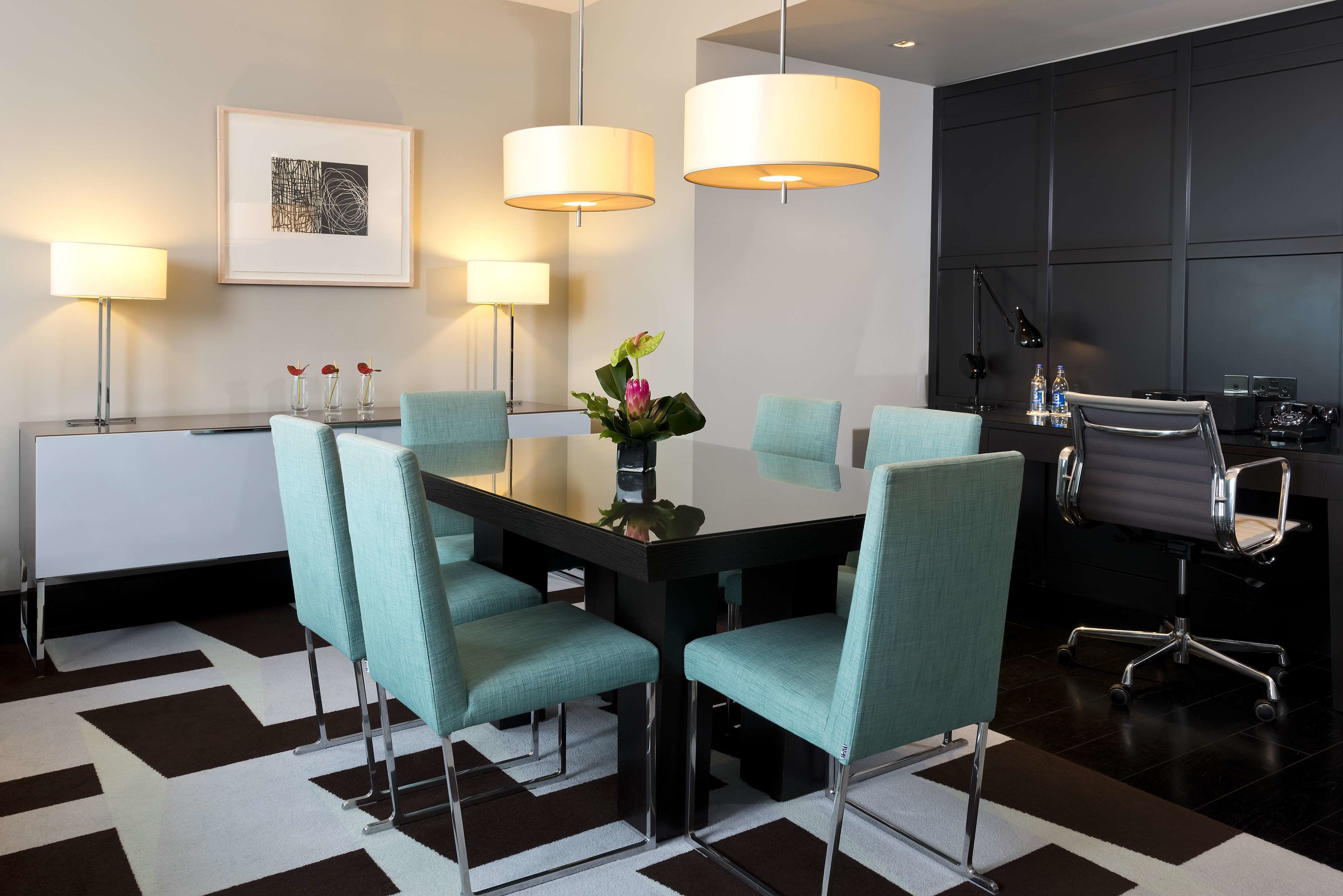 A modern conference room with a black table, teal chairs, and pendant lights.