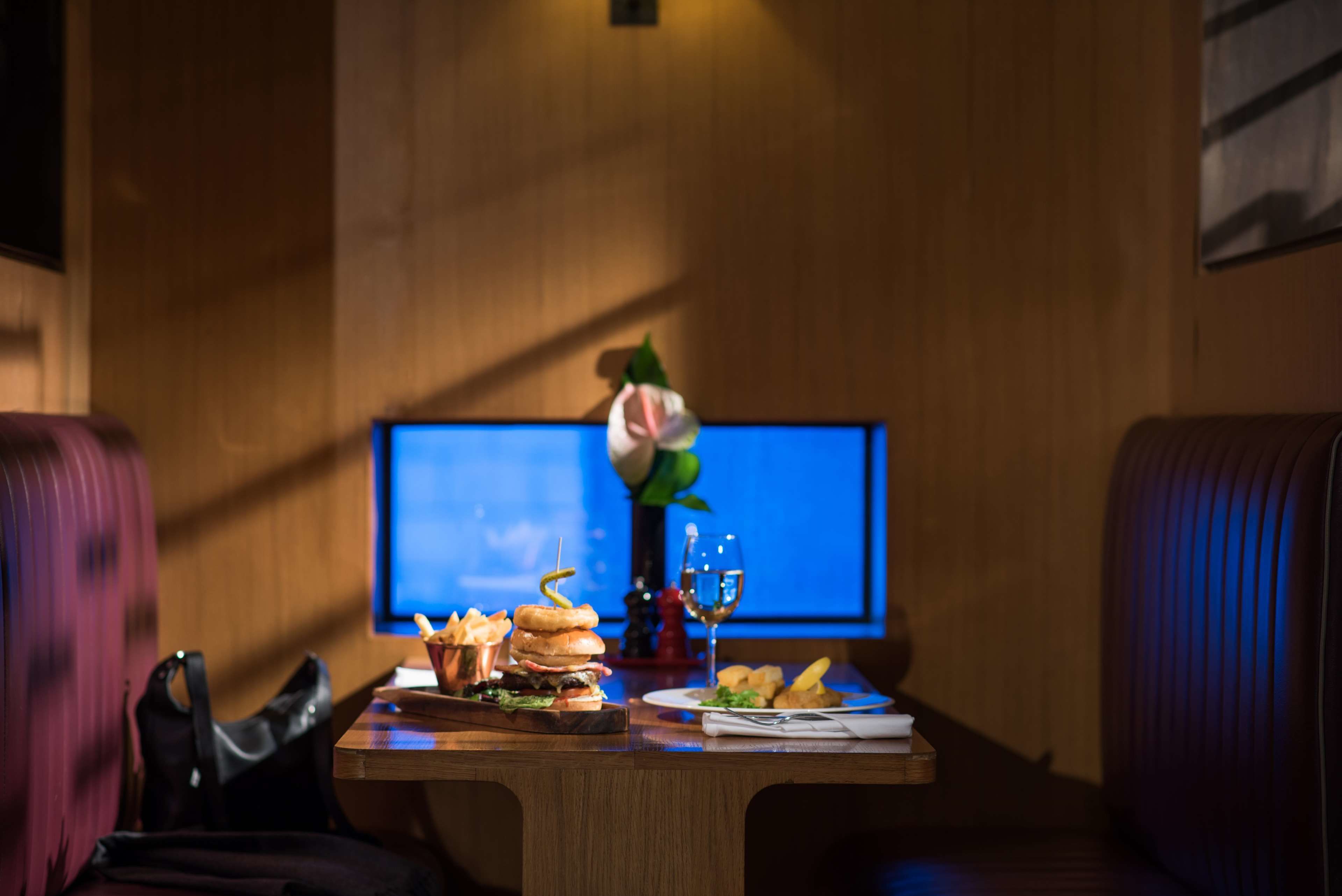 Un comedor con una mesa de madera dispuesta para una comida, un televisor al fondo y una silla roja a la izquierda.