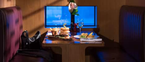 A cozy room with a wooden wall, a television, a table with food, and two leather sofas.