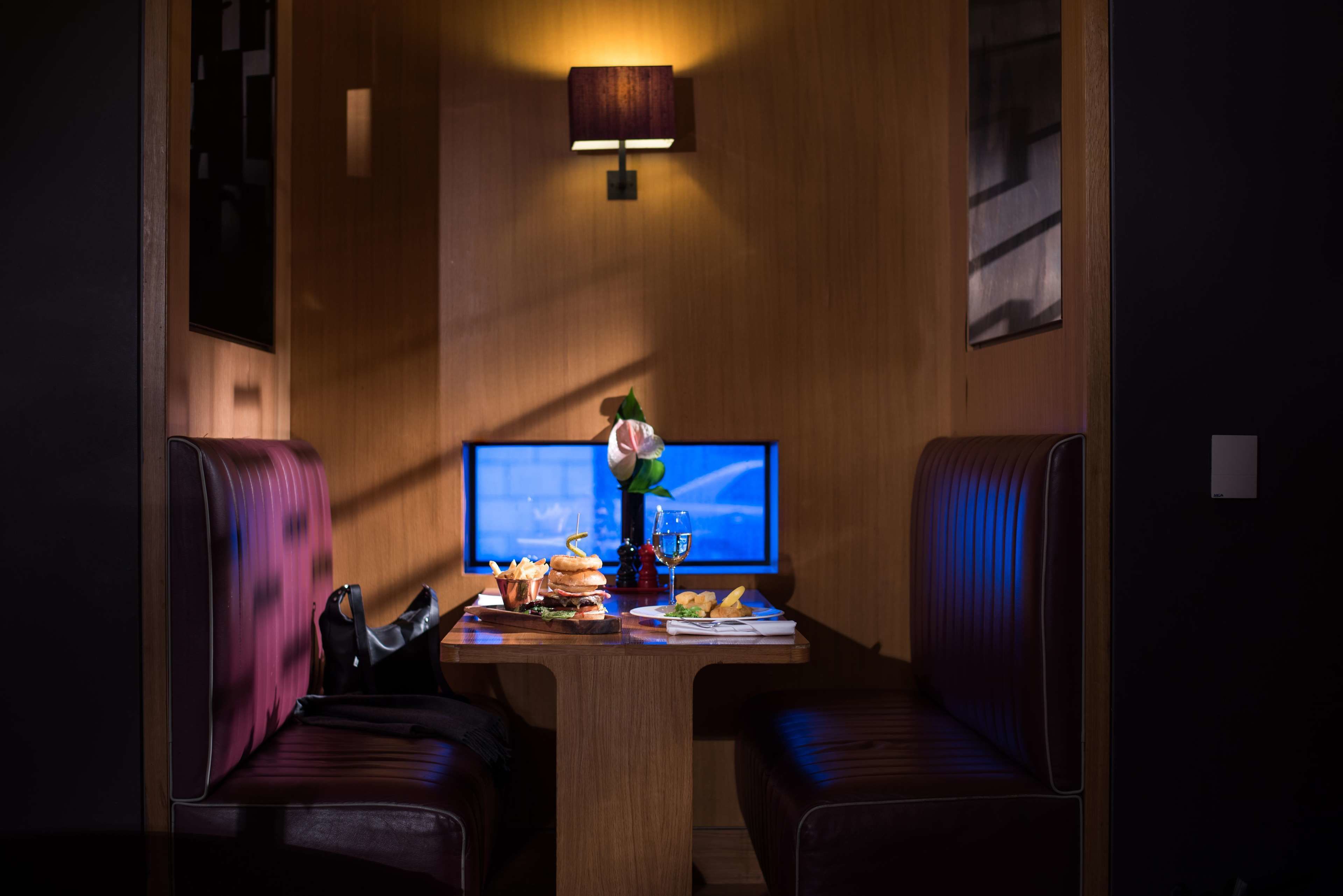 Una habitación tenuemente iluminada con una pared de madera, una mesa con comida y bebidas, y dos sillones de cuero.