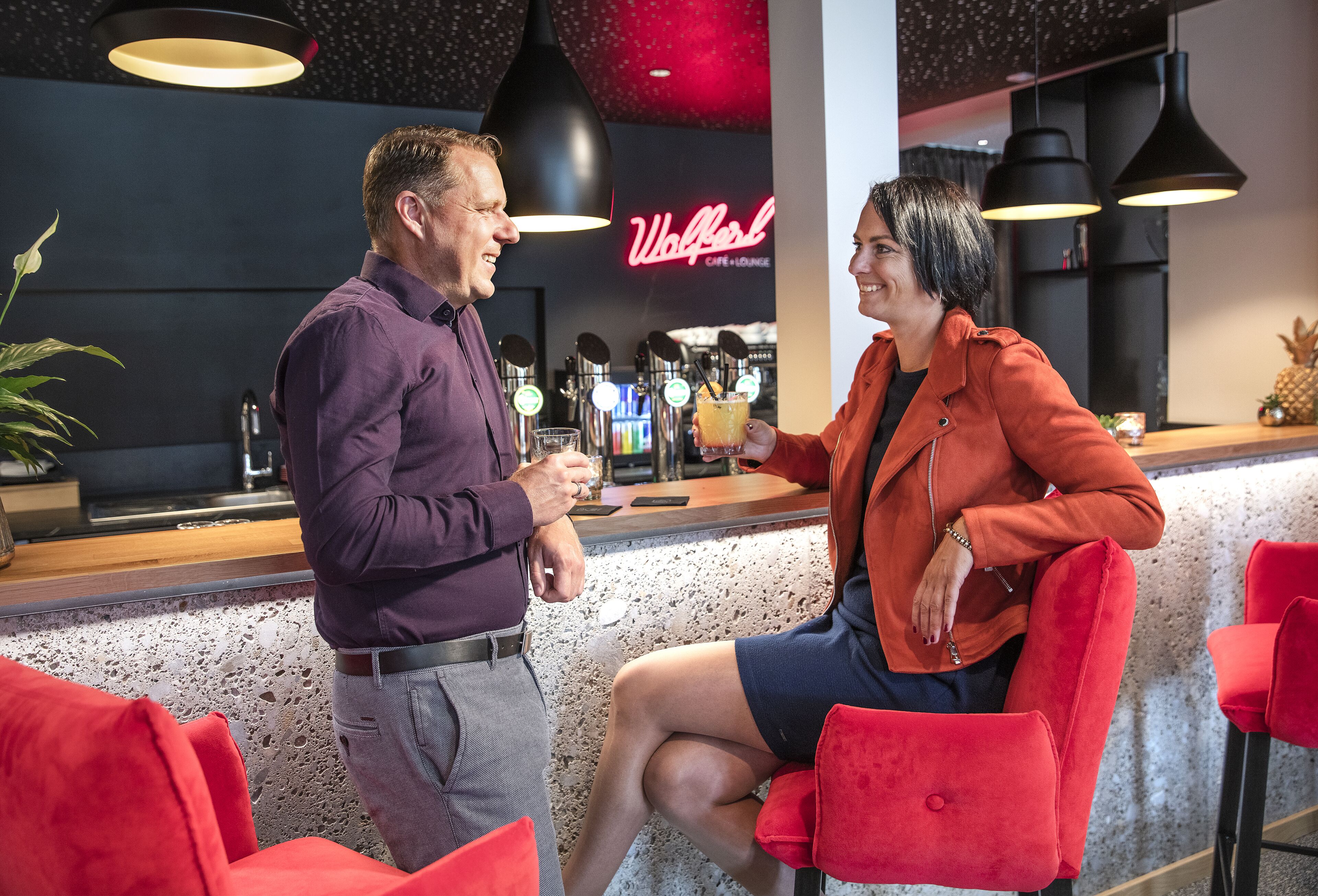 Un homme et une femme sont assis au bar, avec une enseigne au néon en arrière-plan.