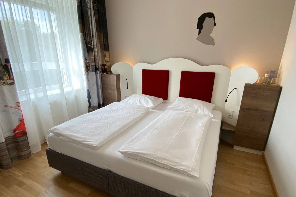 Un lit bien fait, avec du linge de lit blanc, une tête de lit en bois et un panneau décoratif rouge.
