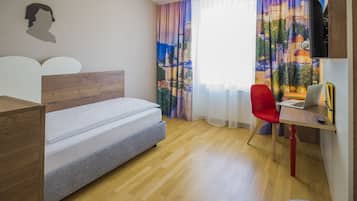 A bedroom with a bed, a desk with a laptop, a red chair, and a TV on a wooden stand.