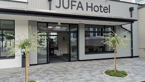 The JUFA Hotel facade with a modern design, large windows, and two small trees in front. - JUFA Hotel Salzburg (Salzburg)