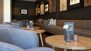 A modern lounge area with sofas, round tables, and framed artwork on the walls. - JUFA Hotel Salzburg (Salzburg)