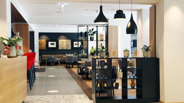 A modern hotel lobby with a reception desk, seating area, and a decorative wall with plants and artwork. - JUFA Hotel Salzburg (Salzburg)