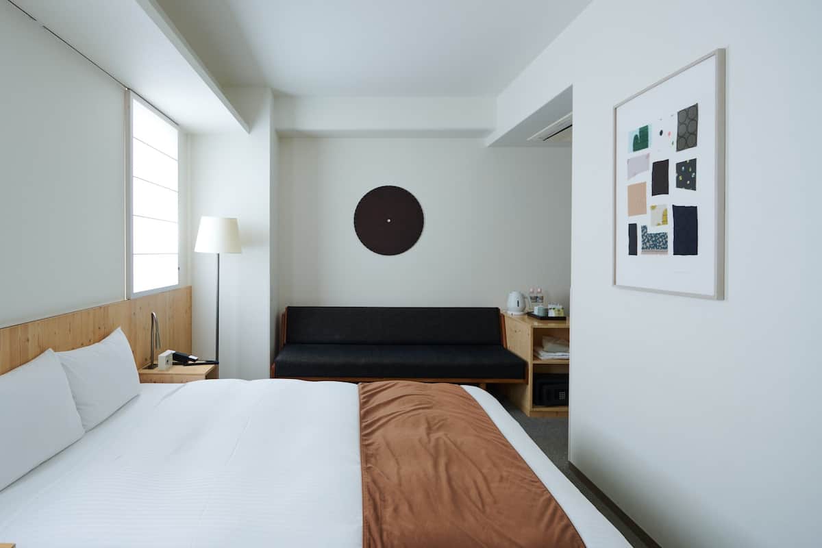 Une chambre d’hôtel comprenant un lit, une table de chevet, une lampe, un canapé et une œuvre d’art accrochée au mur.