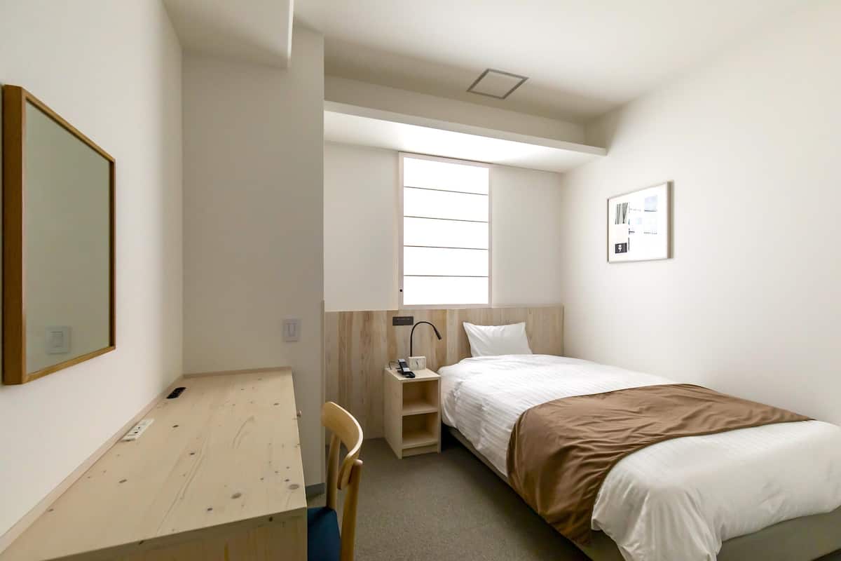 Une chambre d’hôtel de taille réduite, comprenant un lit simple, un bureau et une chaise.