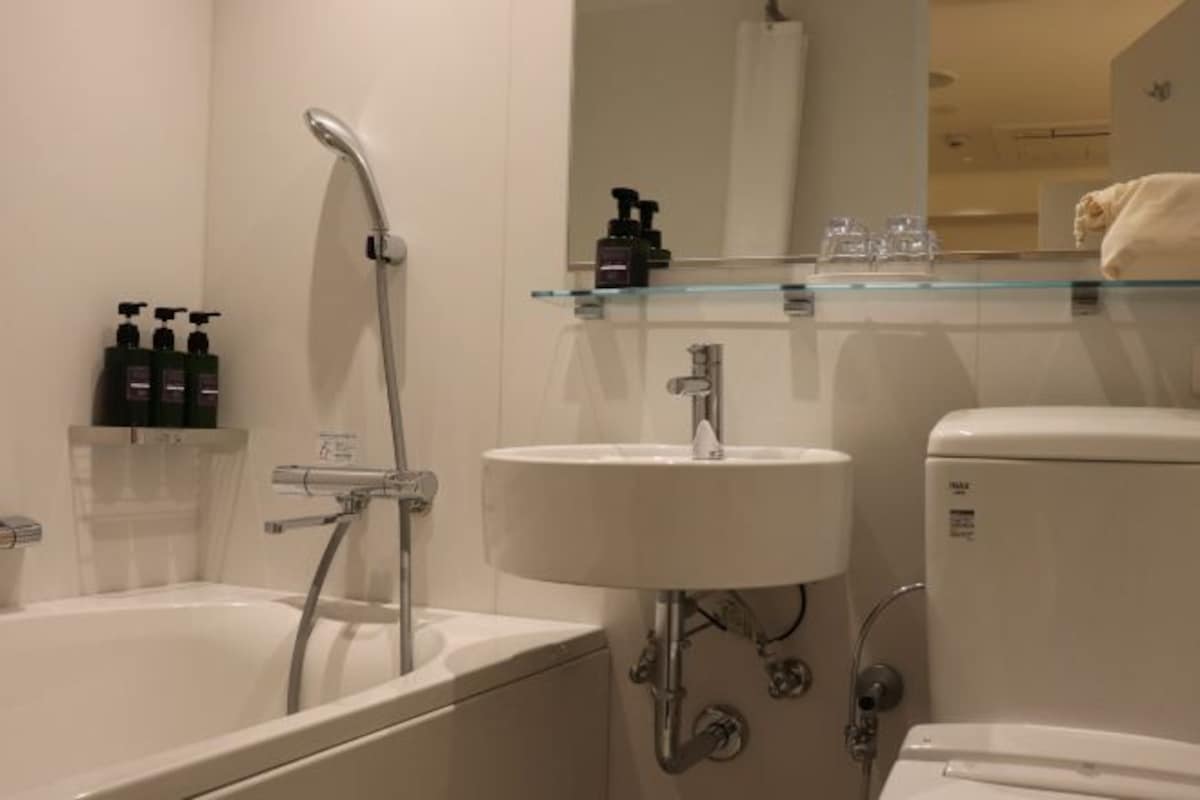 Un baño moderno con bañera, lavabo e inodoro. Hay artículos de aseo en la pared y una repisa de cristal sobre el lavabo.