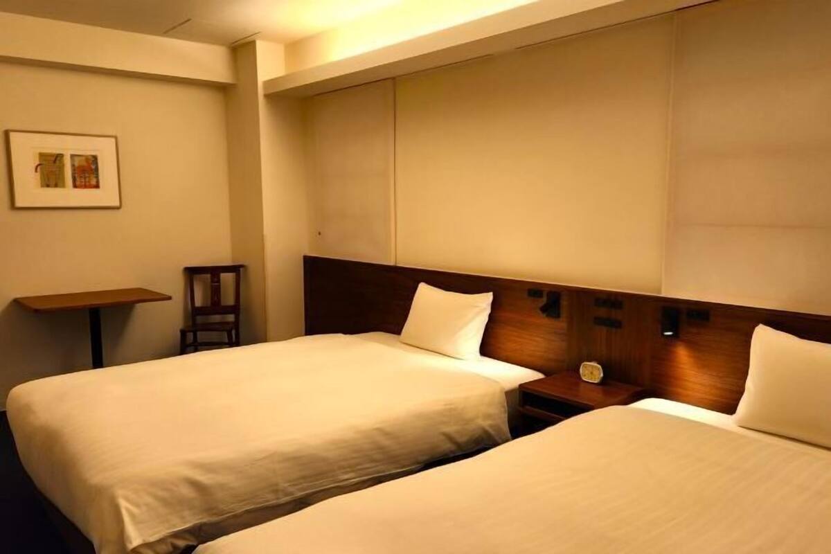 Une chambre d’hôtel avec deux lits, une petite table, une chaise et une horloge fixée au mur.