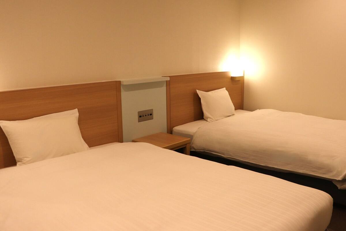 Une chambre d’hôtel avec deux lits, chacun doté de draps blancs et d’une tête de lit en bois. Une table de chevet avec une lampe se trouve entre les deux lits.