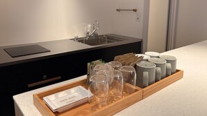 Un coin cuisine comprenant un plan de travail, un évier et un plateau avec des verres transparents et une batterie de vaisselle.
