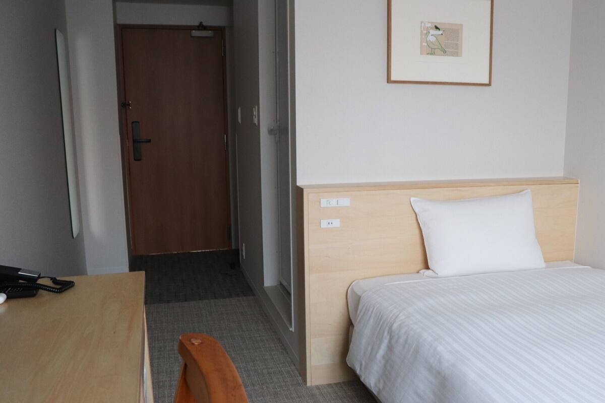 Une chambre d’hôtel avec un lit, un bureau, une chaise, une porte et un tableau encadré au mur.