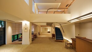 Un intérieur spacieux avec un plafond haut, un escalier reliant les deux étages et un coin salon avec des tables et des chaises.