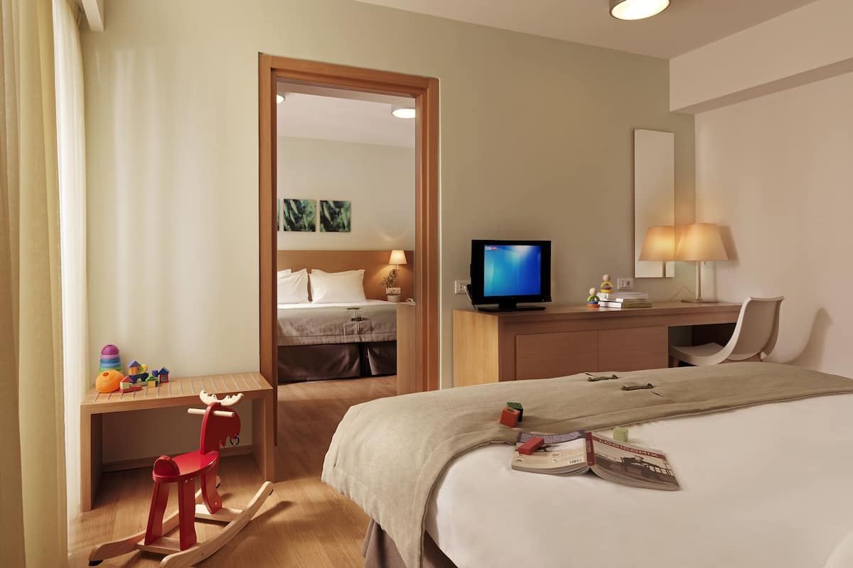 A hotel room with a bed, a desk with a chair, a television, and a mirror.