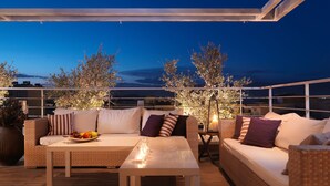 An outdoor seating area with wicker furniture and a table, under a white canopy, overlooking a cityscape at dusk. - Elefsina Hotel (Elefsina)