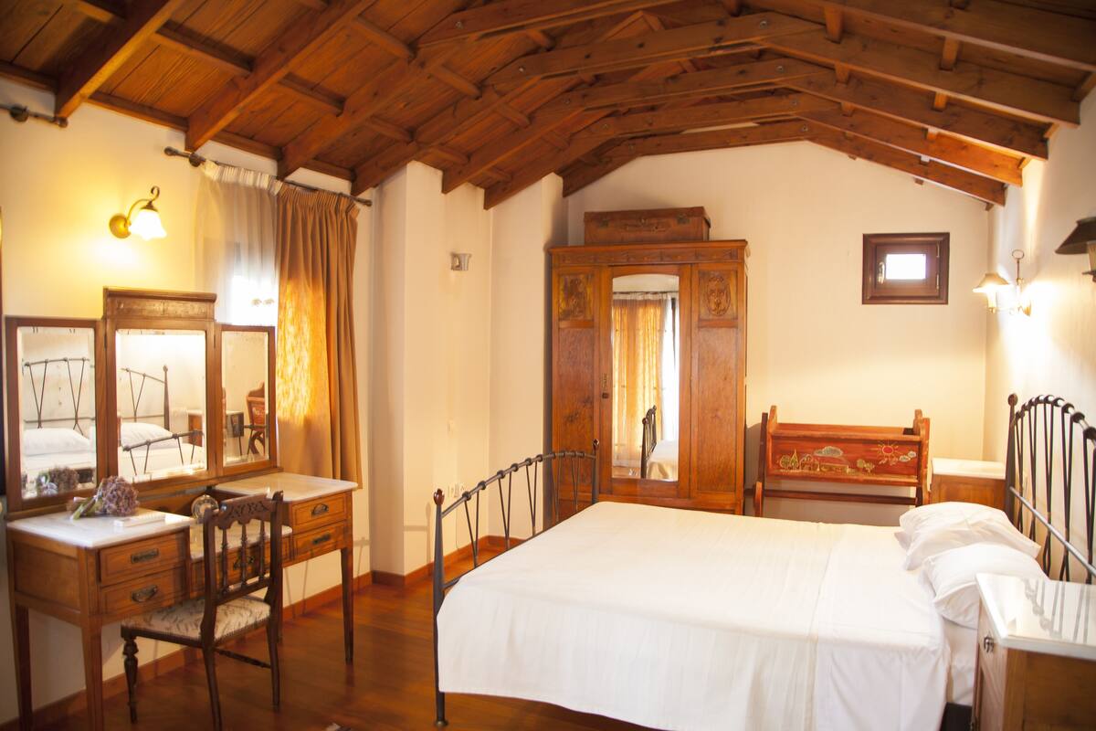 Ein Schlafzimmer mit Holzboden, einem Bett mit weißer Bettwäsche, einer Holzkommode, einem Schreibtisch mit Stuhl und einem Spiegel.