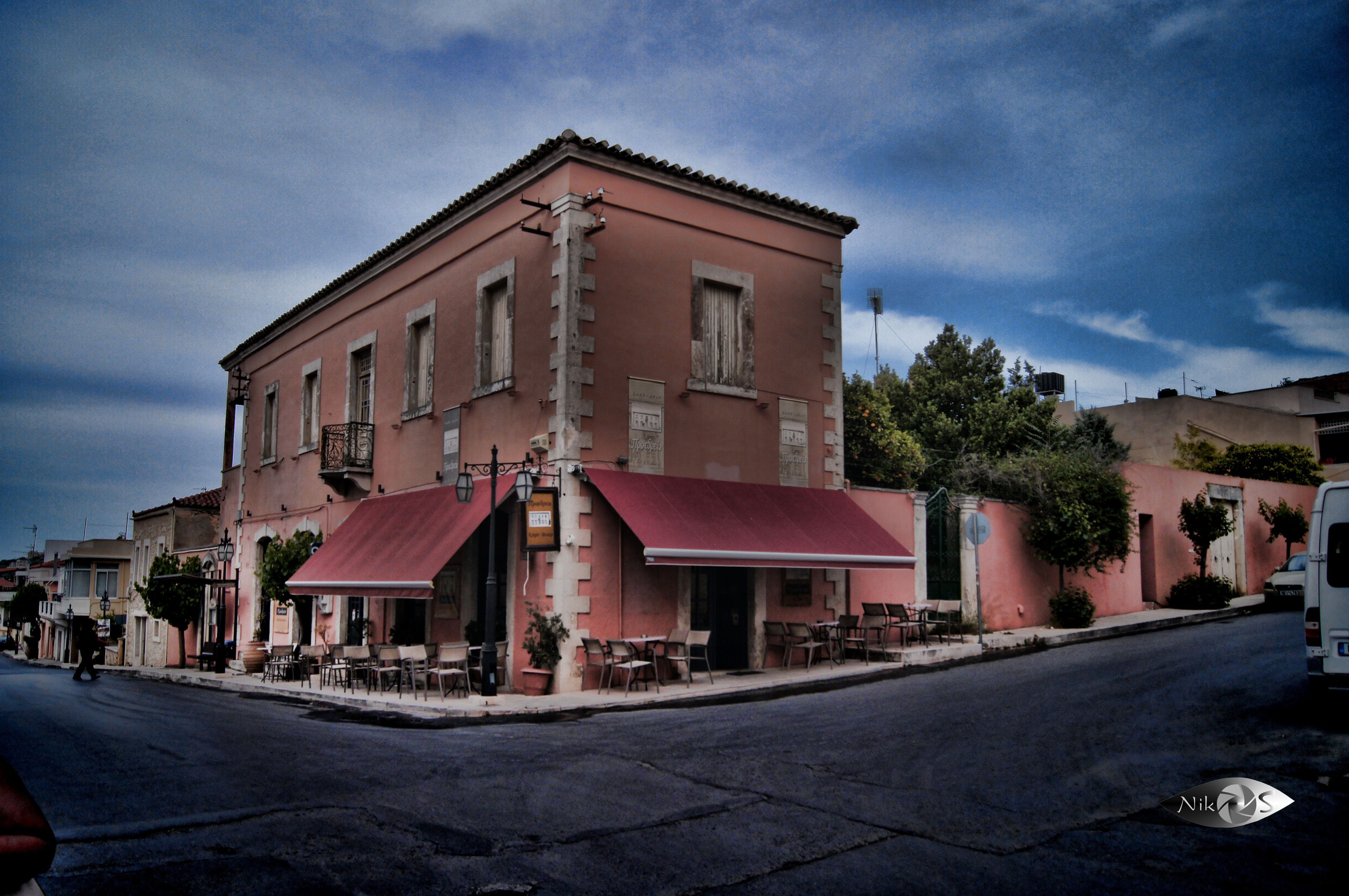 A pink building with a red awning, outdoor seating, and a visible sign.