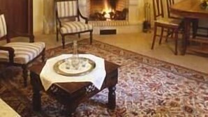 Un salon chaleureux avec une cheminée, des poutres apparentes en bois au plafond et un tapis à motifs.