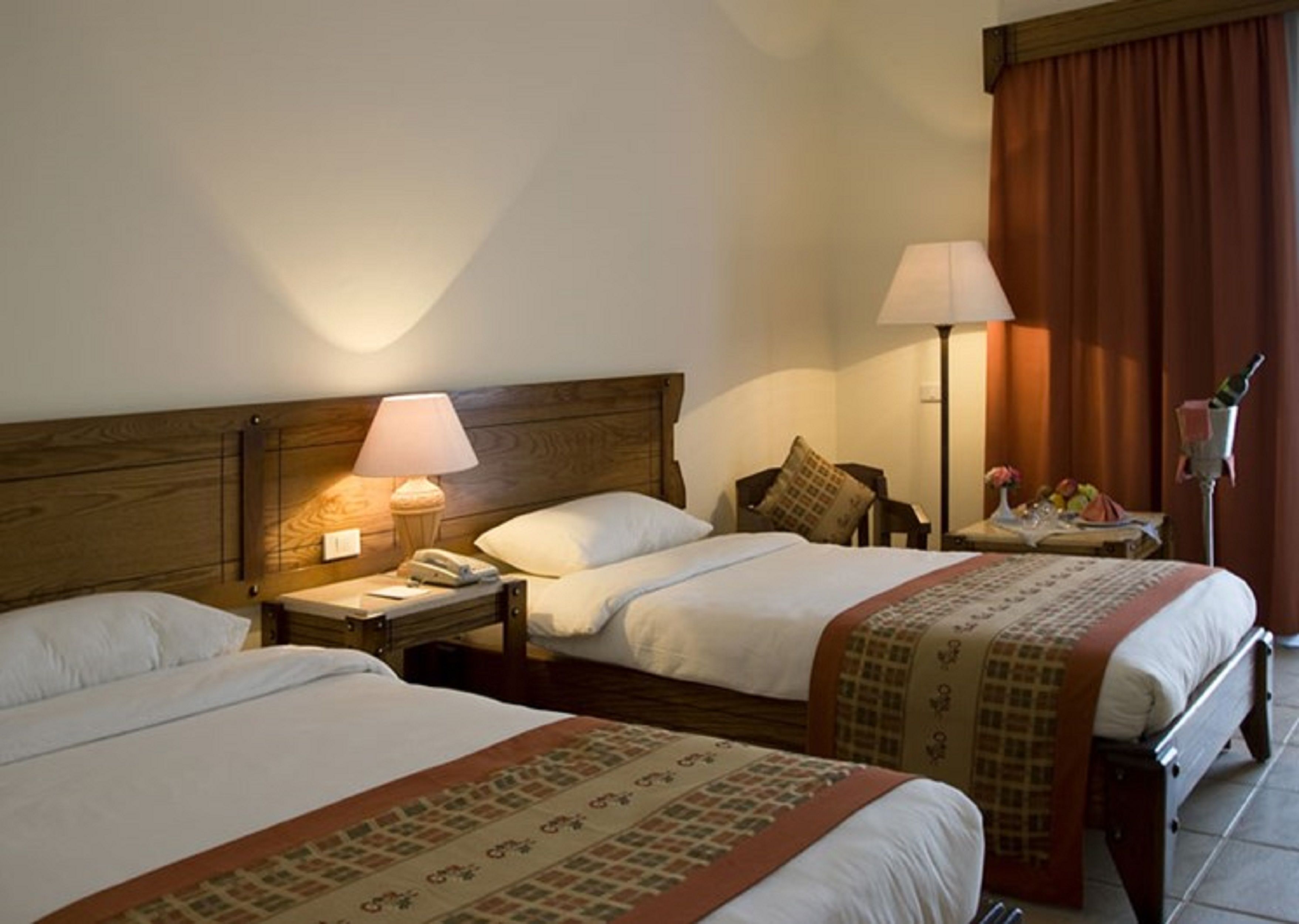 A hotel room with two beds, a nightstand with a lamp, a telephone, and a small table with a vase of flowers.