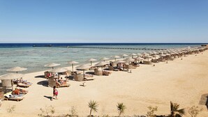 Ein Strand mit Reihen von Liegestühlen und Sonnenschirmen, ein Steg, der ins Meer führt, und ein klarer, blauer Himmel.