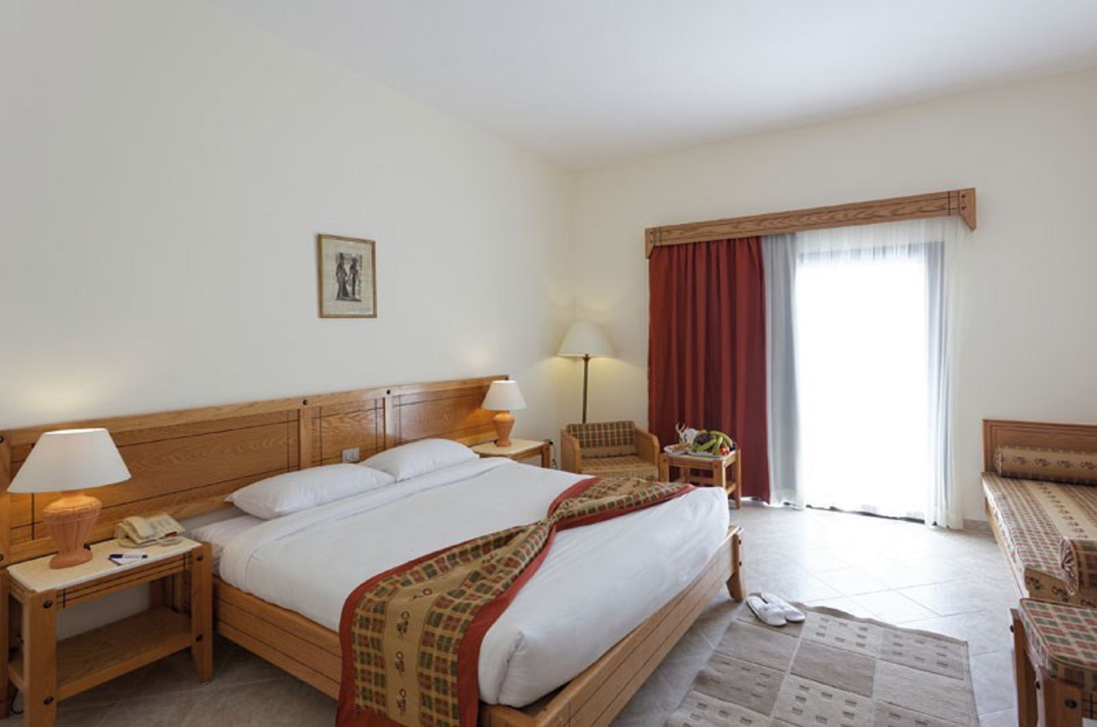 A hotel room with a large bed, two bedside tables with lamps, a chair, a sofa, and a window with curtains.
