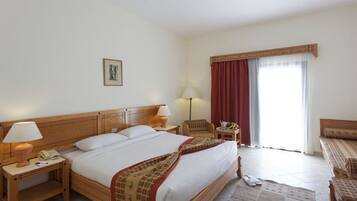 A hotel room with a large bed, two bedside tables with lamps, a chair, a sofa, and a window with curtains.