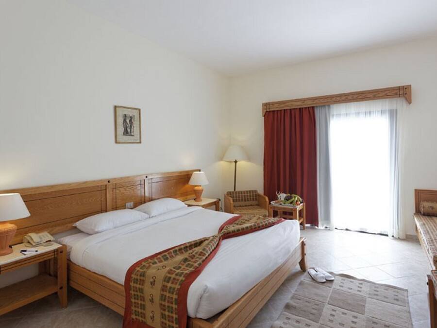 A hotel room with a large bed, two bedside tables with lamps, a chair, a sofa, and a window with curtains.
