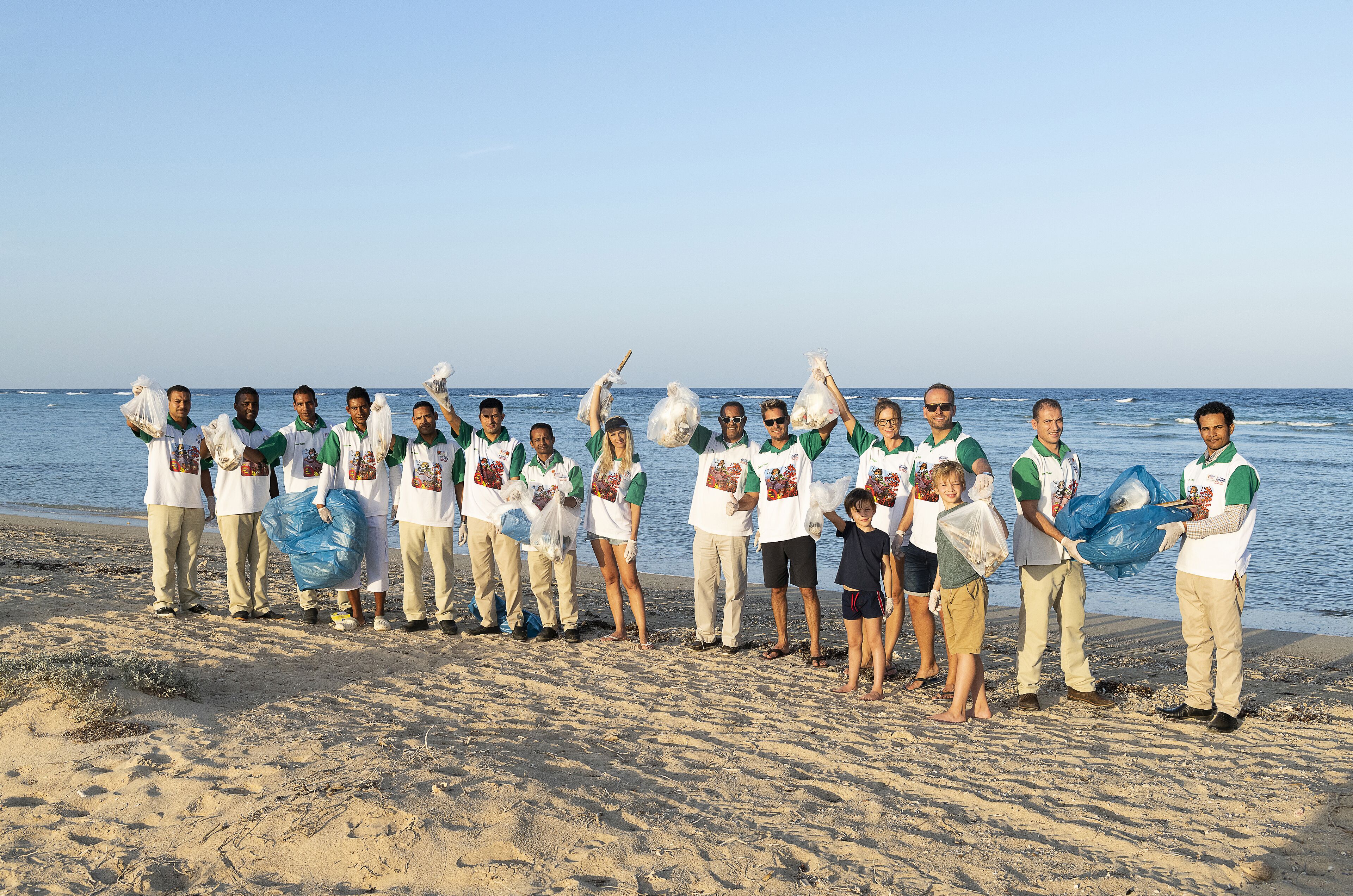 A group of people on a beach holding bags, possibly for a beach cleanup event.