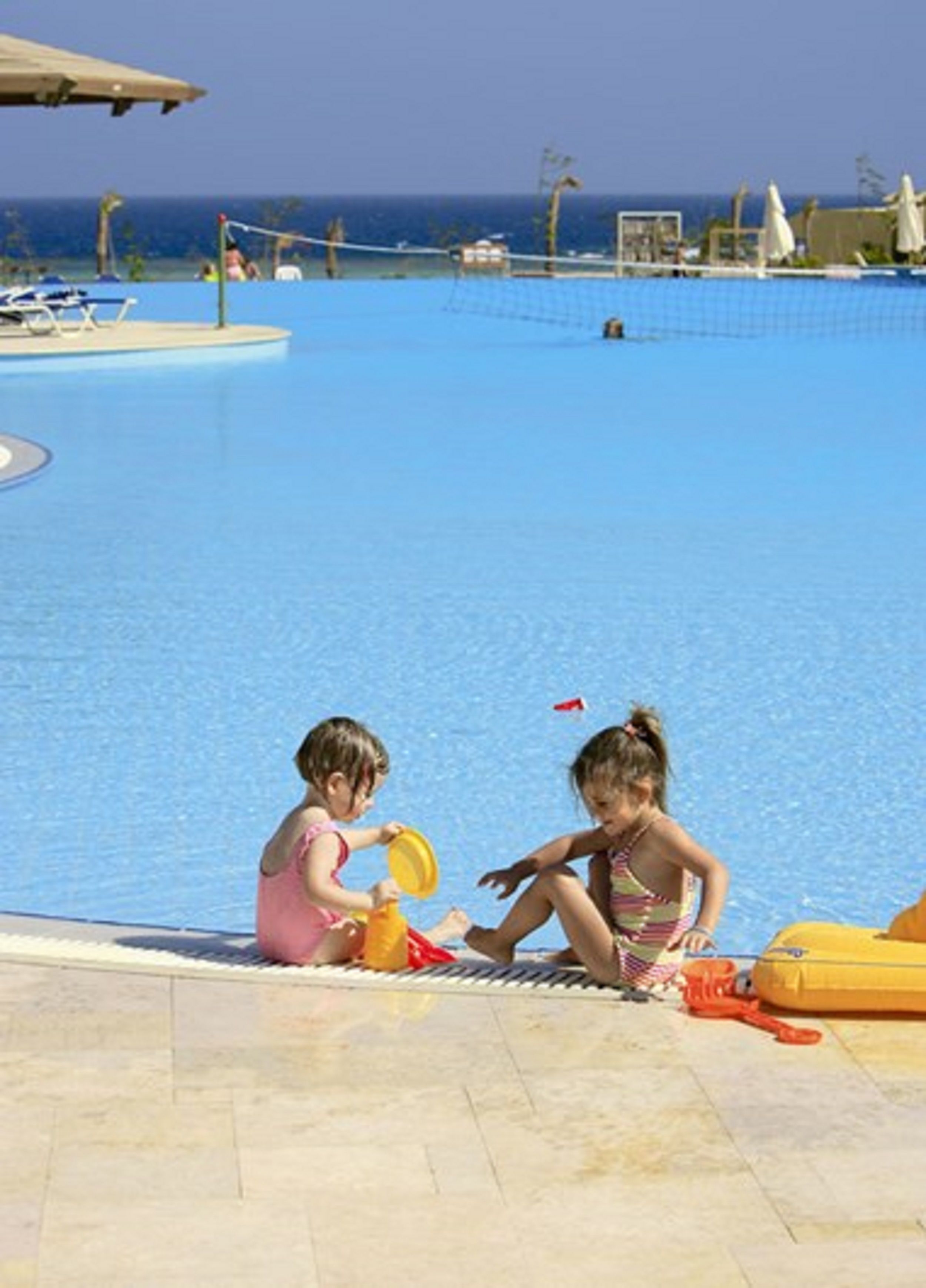 Two children playing near a pool with a view of the ocean.