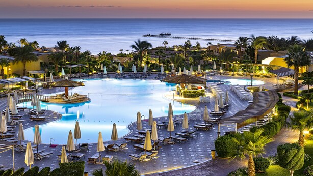 Ein Resort mit großem Schwimmbad, Liegestühlen, Sonnenschirmen und Meerblick.