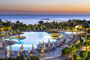 Ein Resort mit großem Schwimmbad, Liegestühlen, Sonnenschirmen und Meerblick.