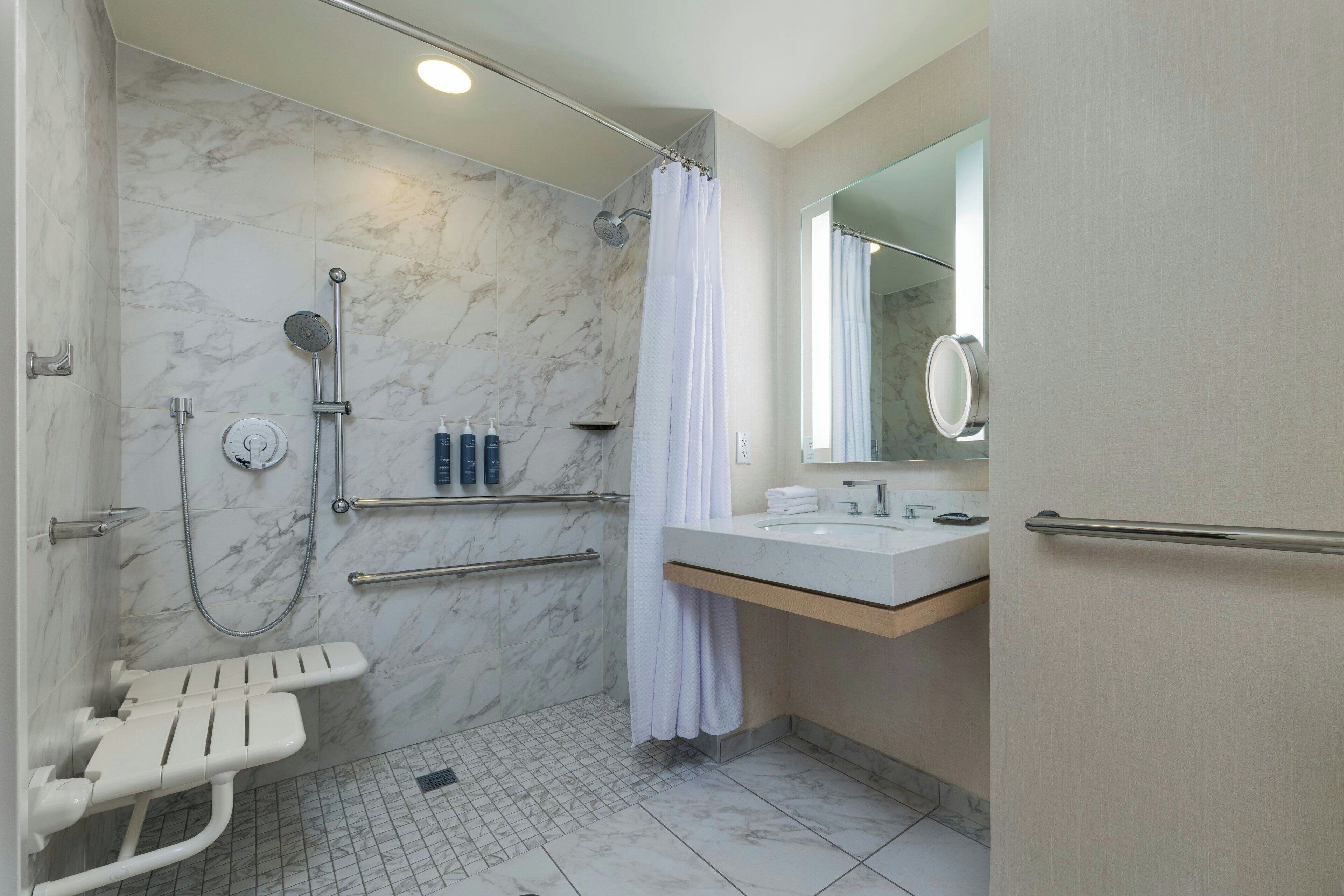 A modern bathroom with a shower, a toilet with a grab bar, a sink, and a mirror.