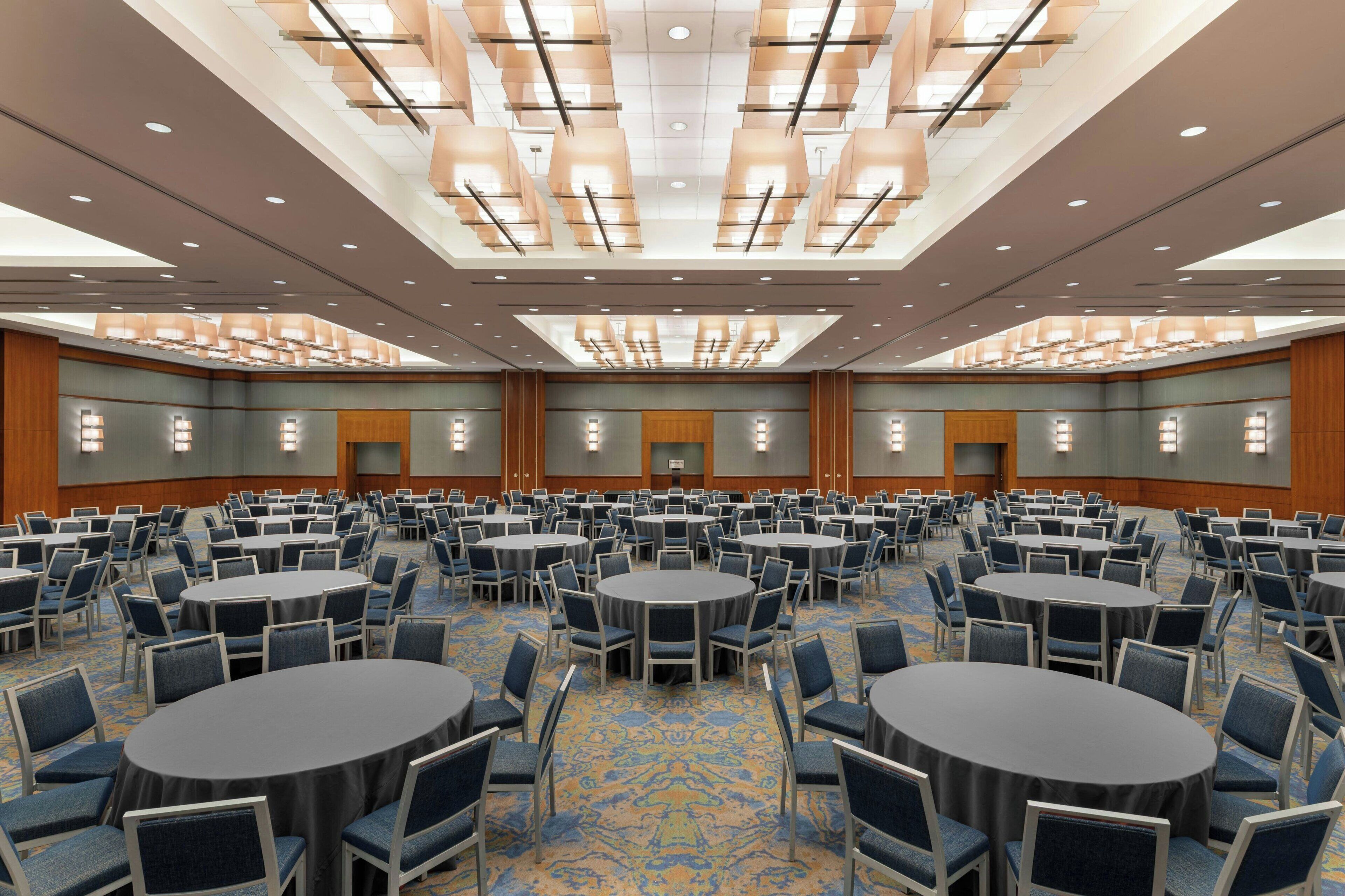 A large conference room with multiple round tables and chairs, a patterned carpet, and a high ceiling with recessed lighting.