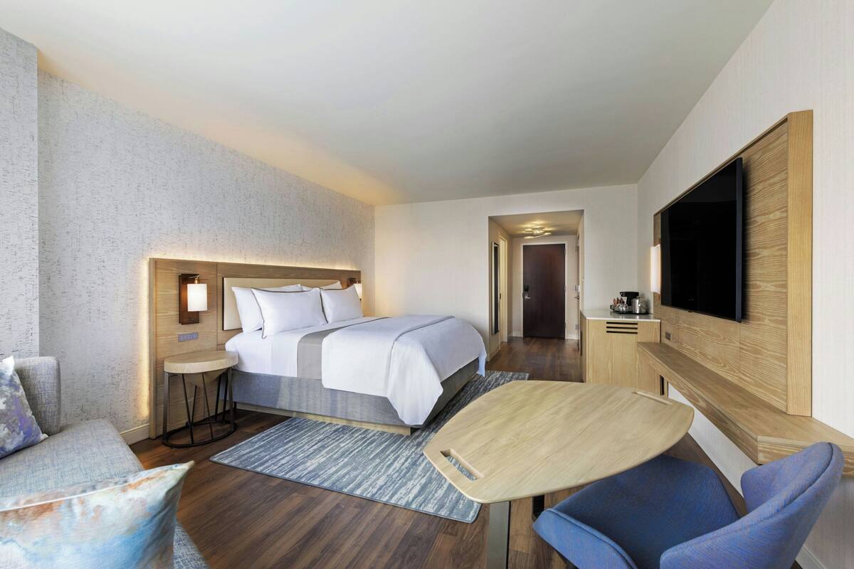 A hotel room with a bed, a TV, a small table, a chair, and a desk.