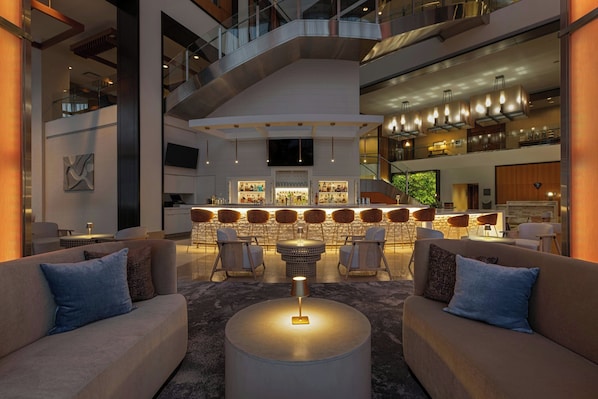 A modern interior with a central bar area, seating arrangements, and a staircase.